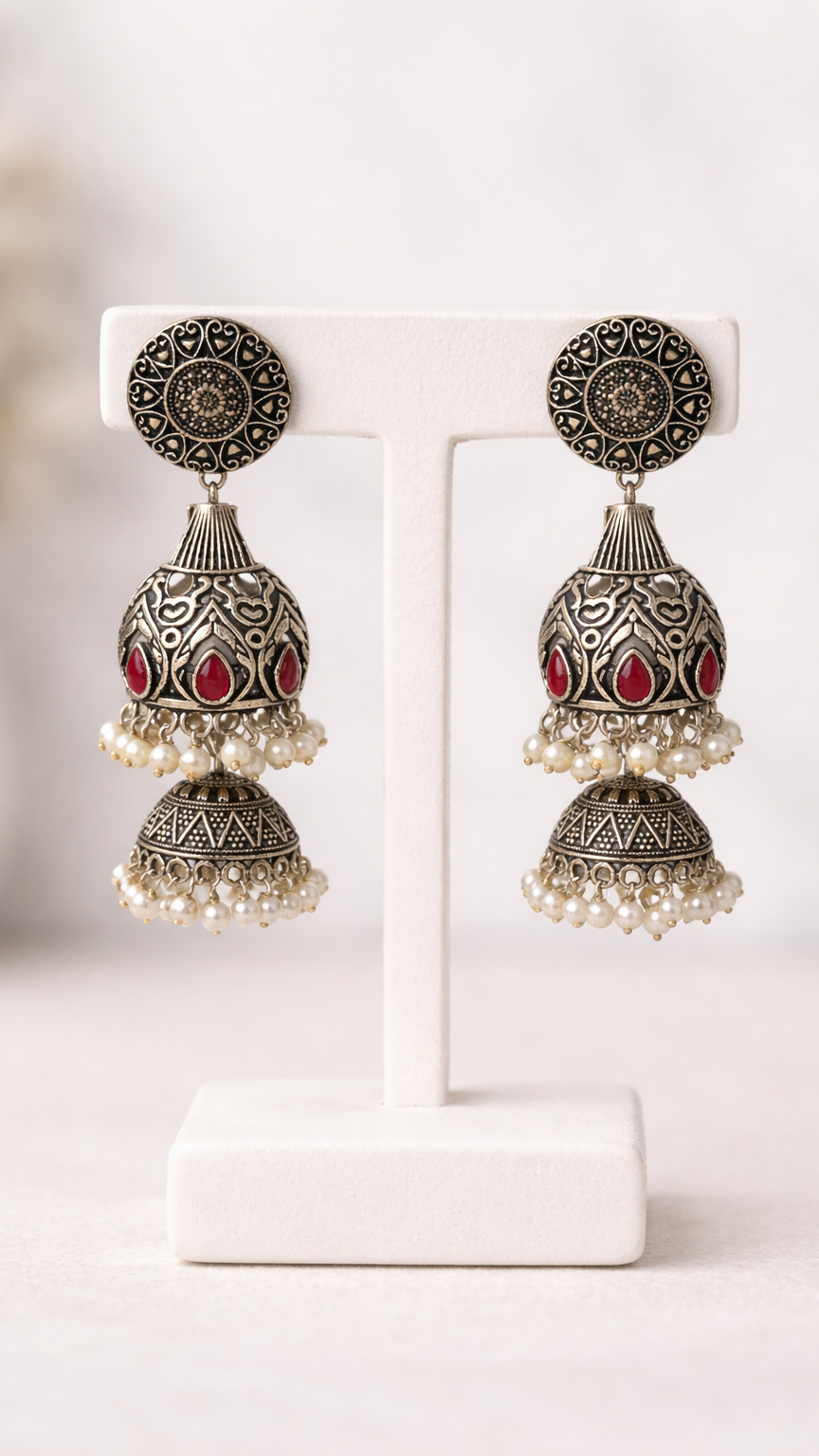 Boucles d'oreilles argentées en métal gravé, ornées de pierres rouges et d'une bordure en perle blanche.